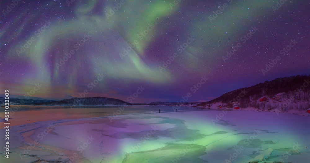 Panoramic view at fjord with coast of the Norwegian Sea in the background snowy mountains Arctic Circle - Northern lights or Aurora borealis in the sky over Tromso, Norway