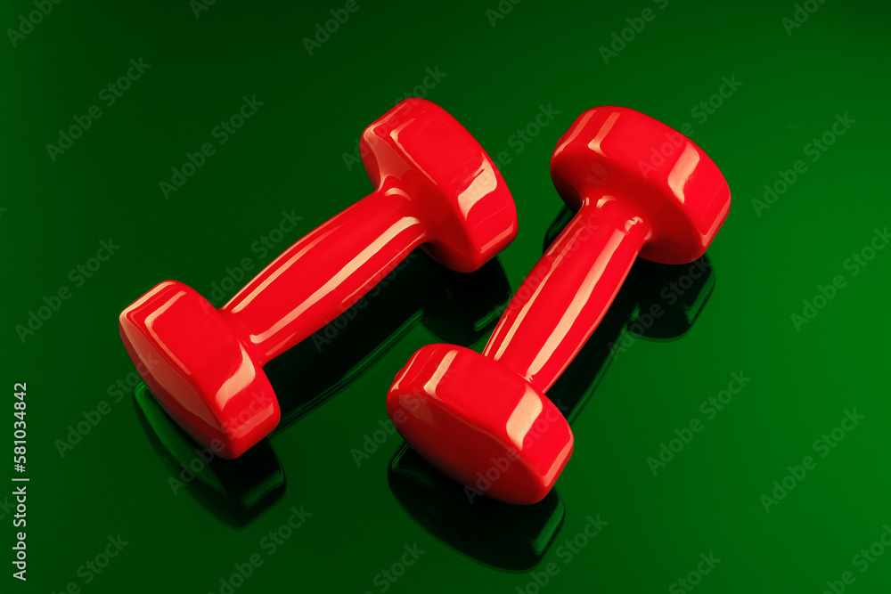 A pair of red dumbbells is reflected in a green glass surface. View from above. A pair of red dumbbells is reflected in a green glass surface. View from above.