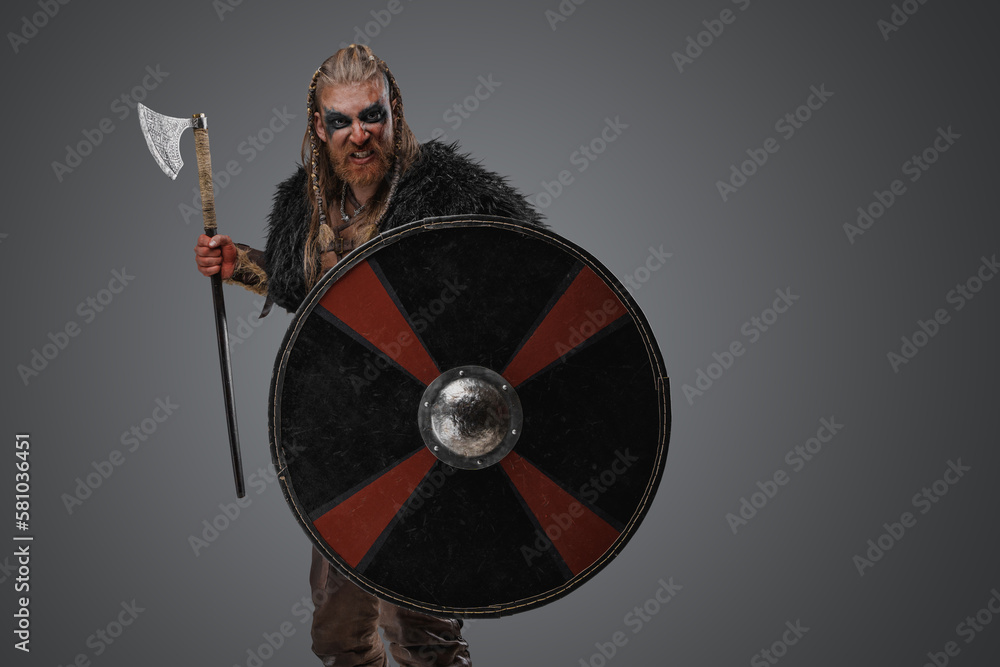 Naklejka premium Studio shot of isolated on gray background viking with black fur holding shield and axe.