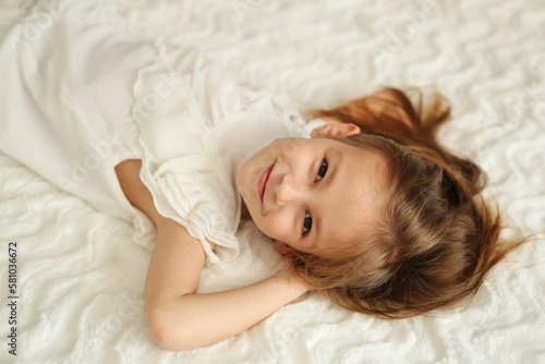 A girl in a white dress is lying on a white bed
