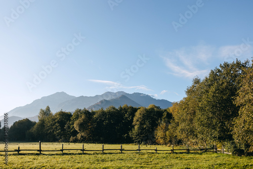 Canvas Print Backyard view over a green lawn in morning sun light with mountains on background