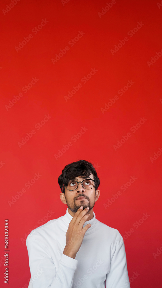 Curious face. Idea consideration. Option decision. Portrait of pensive puzzled smart man in glasses thinking on red color copy space advertising background. Curious face. Idea consideration. Option decision. Portrait of pensive puzzled smart man in glasses thinking on red color copy space advertising background.