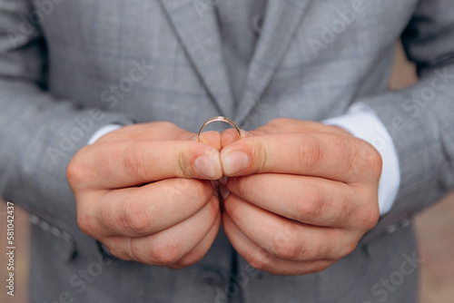 Close-up photo of the groom's hands holding the wedding ring with both hands. Wedding ring before the proposal. A man gets married