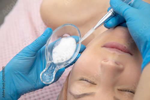 Cropped cosmetologist hands in blue gloves applying white benzoyl peroxide powder with spatula, facial chemical cream photo