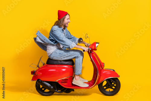 Full length photo of positive impressed man wear denim looking emtpy space riding moped isolated yellow color background © deagreez