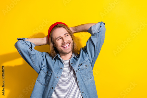 Portrait of cheerful positive man with bob haircut wear denim jacket look empty space arms behind head isolated on yellow color background © deagreez