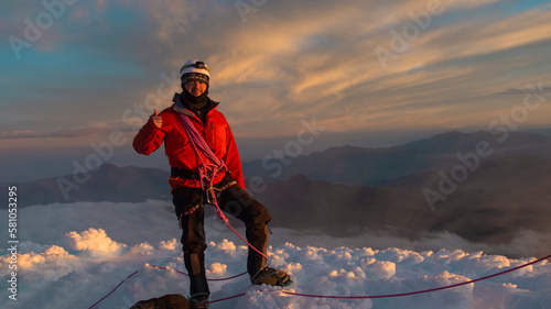 Young male climber standing on the summit of Cotopaxi volcano during a cloudy sunrise