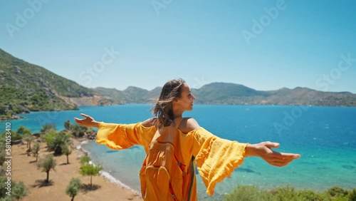 rear view attractive slim tanned woman traveler in orange sundress stands on shore of beautiful bay with turquoise water and paradise empty sea beach. Girl walks at sea coast in Turkey, photo