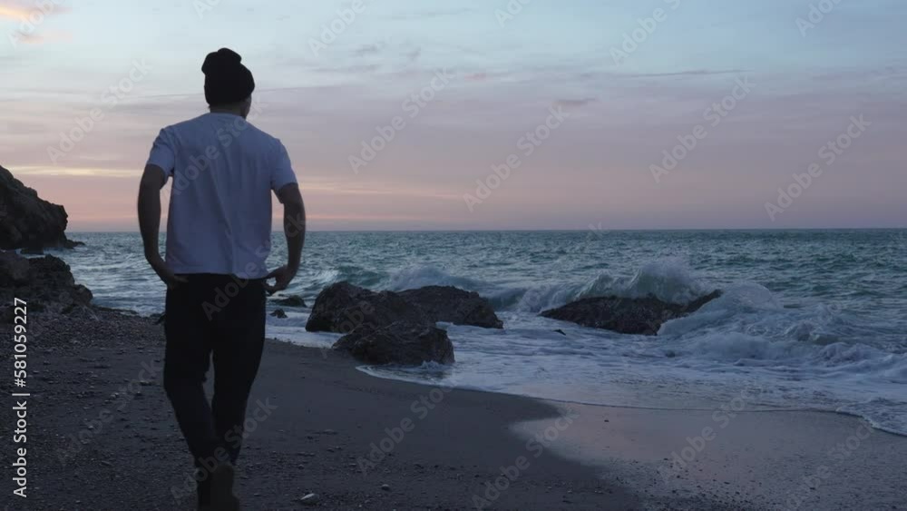 Man in white shirt walks along the ocean coast during nightfall, takes photo of sea Man in white shirt walks along the ocean coast during nightfall, takes photo of sea