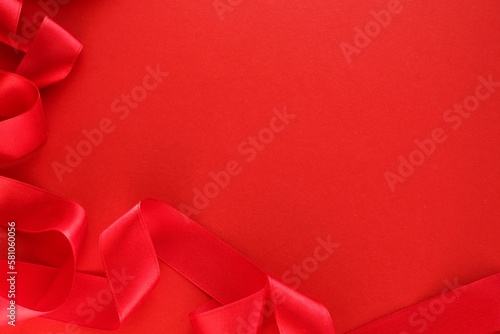 Curved wavy silk satin red ribbon on red background with copy space for text. Holiday, celebration, anniversary, birthday gift decoration concept. Idea for greeting card, sale banner
