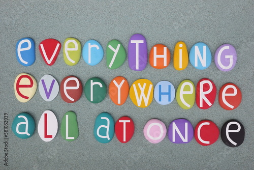 Everything, everywhere, all at once, creative slogan composed with multi colored stone letters over green sand photo