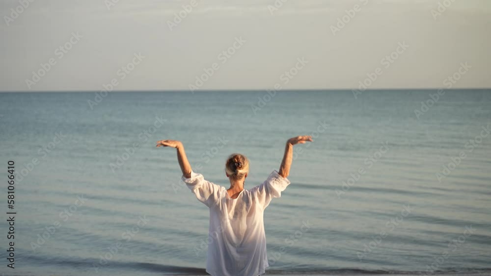 Back of fit slim mature senior woman stretching doing yoga during the morning sunrise on the tropical beach. Back of fit slim mature senior woman stretching doing yoga during the morning sunrise on the tropical beach.