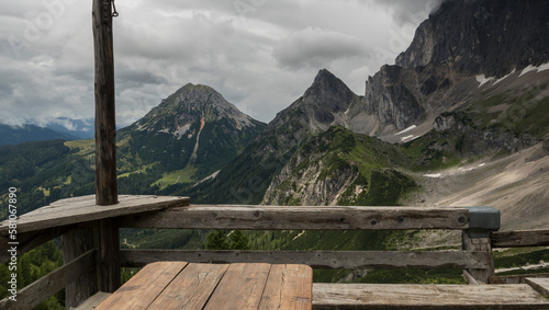 View from the terrace of the Südwandhütte Austrian alpine mountain hut towards the valley surrounded with beautiful mountains. In the foreground a wooden fence and a wooden table.