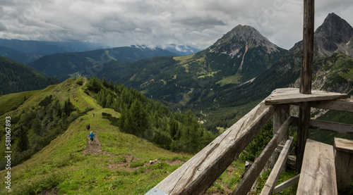 View from the terrace from the Südwandhütte towards the valley with some hikers on a mountain ridge in Austria in the Dachstein mountains during summer.