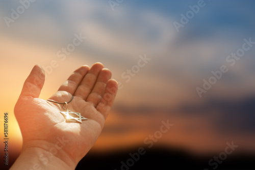 Foto Closeup of pendant in the shape of the star of david on the hand of a man on sunset sky background