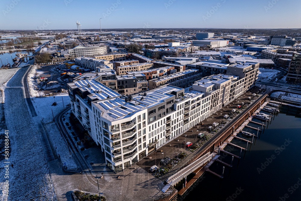 Winter aerial scene with luxury apartment building in the foreground covered in snow next to recreational port Zutphen. Residential real estate concept.