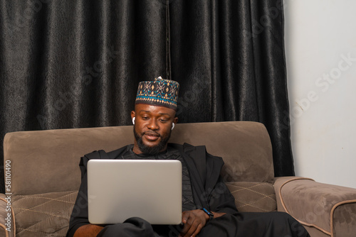 Good looking businessman in Africa attire seated using his laptop to perform business transactions