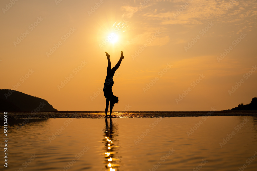 Silhouette woman is play yoga exercise on stone near the beach with sunset time