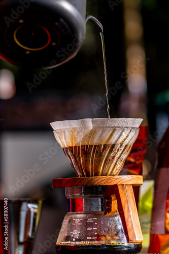 Professional barista pour hot water over the coffee powder  in a filter on chemex pour over coffeemaker and drip kettle. Hand drip coffee concept. photo