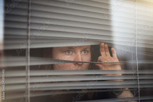 Blond man peeking through window blinds photo
