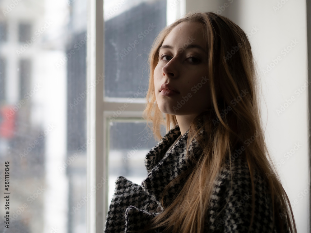 Close up portrait of a beautiful young woman with long natural blonde hair and smooth skin against a window Close up portrait of a beautiful young woman with long natural blonde hair and smooth skin against a window