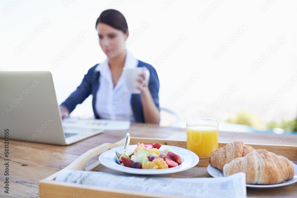 Checking her e-mails before breakfast. An attractive young woman working on her laptop with her breakfast in focus.