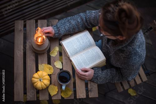 Still autumn life with books and coffee. The girl is sitting at the table with a book next to a lamp and a pumpkin.