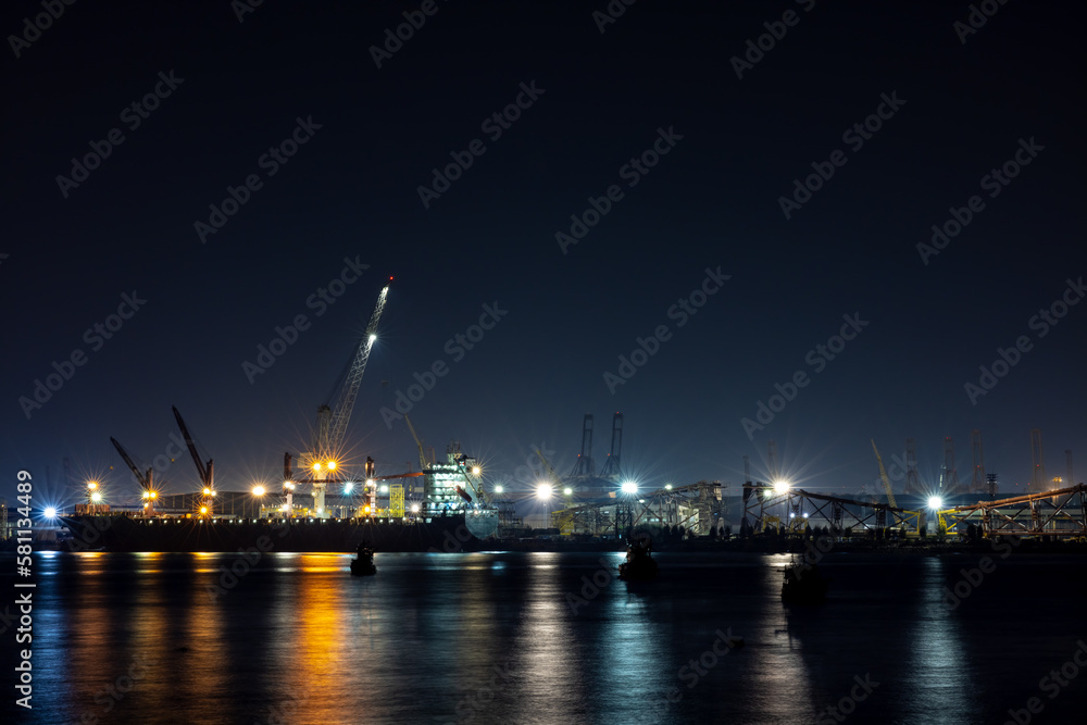 shipyard dry dock maintenance and repair container ship transport and oil ship tanker, crane work and commercial port reflection in water, business and industry zone at night over lighting 