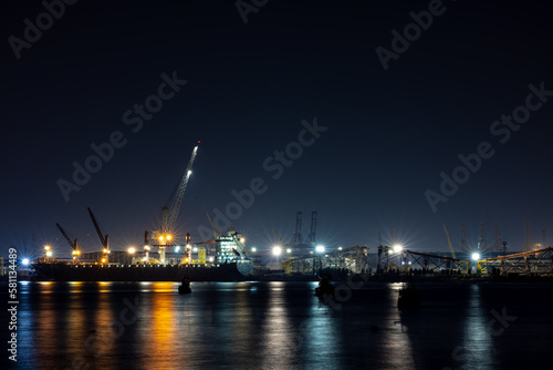 shipyard dry dock maintenance and repair container ship transport and oil ship tanker, crane work and commercial port reflection in water, business and industry zone at night over lighting 