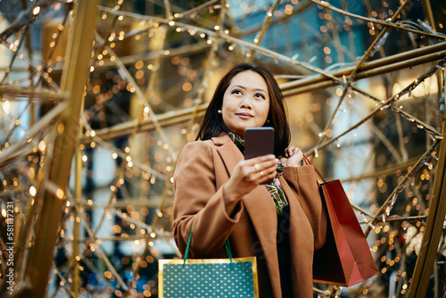 Asian woman using cell phone while shopping in city and looking away. photo