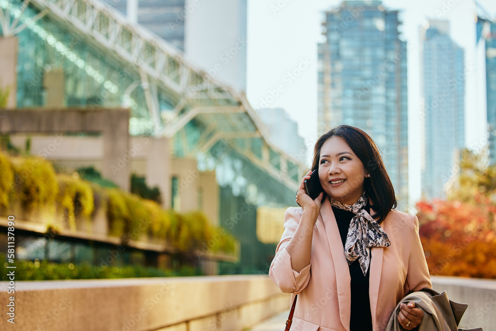 Happy Asian businesswoman talks on cell phone in city,