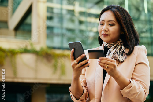 Asian female entrepreneur using credit card and smart phone in city.