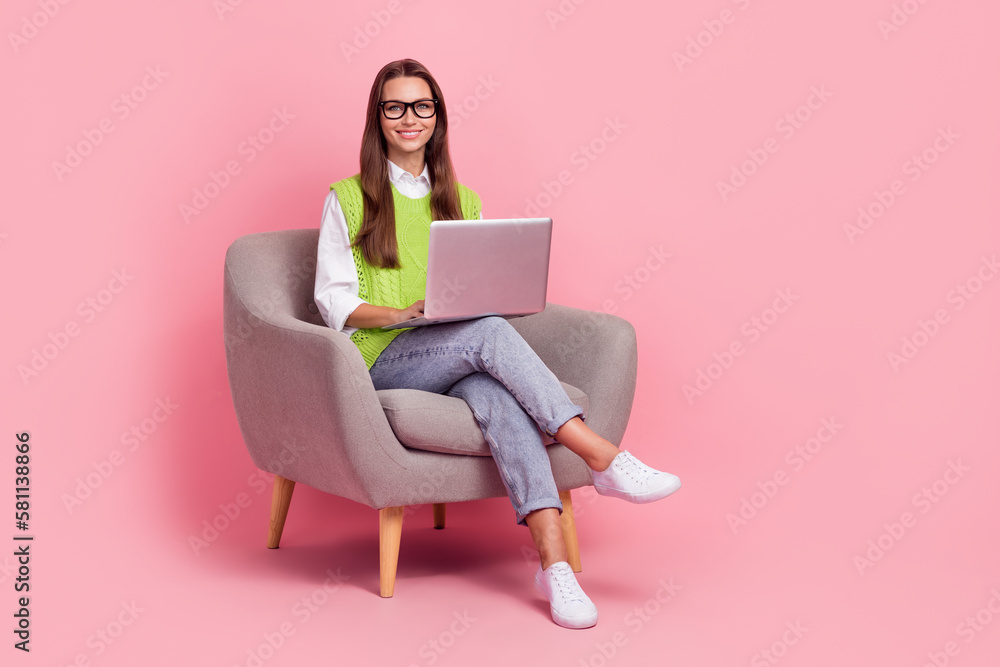 Full length photo of optimistic cheerful girl with straight hairdo dressed green vest writing on laptop isolated on pink color background Full length photo of optimistic cheerful girl with straight hairdo dressed green vest writing on laptop isolated on pink color background