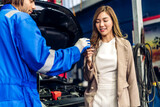 Professional car technician mechanic in uniform work fixing vehicle car engine and maintenance repairing show car report and give car key to customer in auto service. Automobile customer service
