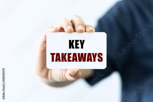 Key takeaways text on blank business card being held by a woman's hand with blurred background. Business concept about key takeaways.