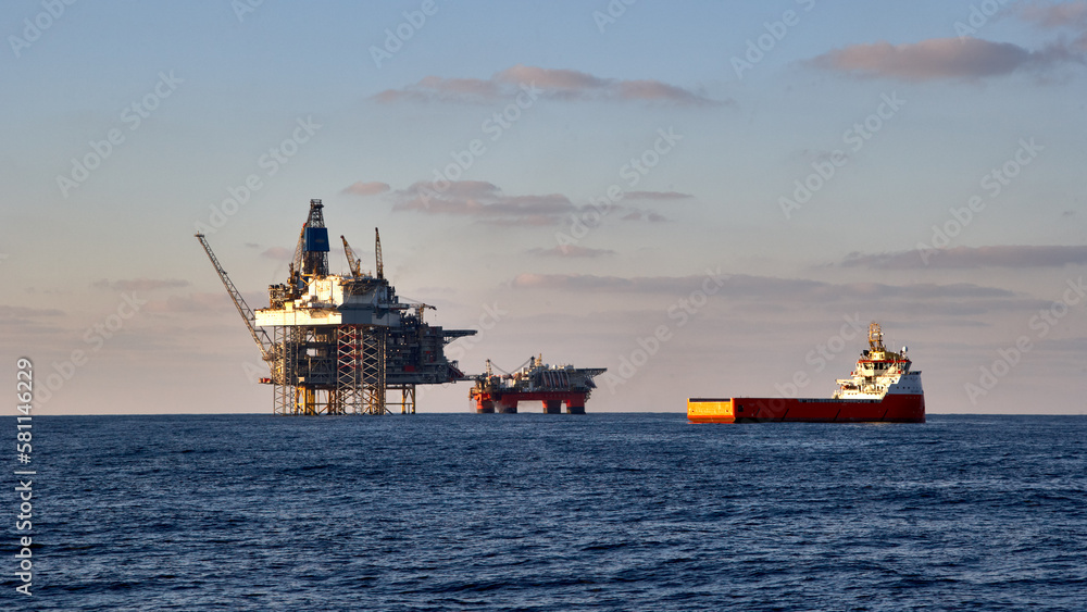 View of jack up drilling rig, platform in the sea with supply vessel in fore ground. Oil and gas production in the sea, ocean.
