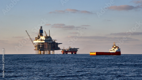 View of jack up drilling rig, platform in the sea with supply vessel in fore ground. Oil and gas production in the sea, ocean.