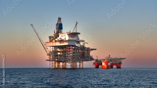 Crude oil production in the sea. View of jack up rig, semi submersible platform and supply vessel in the ocean in sunset sky. 