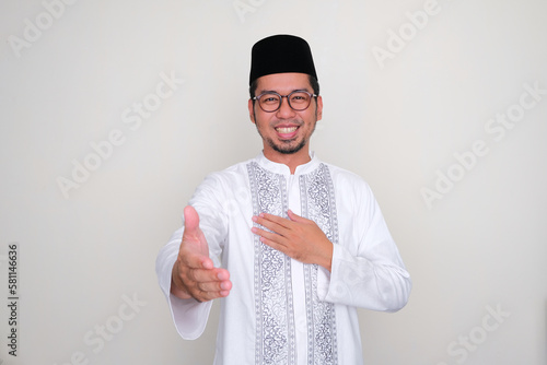 Moslem Asian man smiling friendly while offering a handshake photo