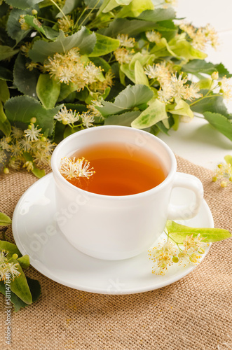 Herbal tea with lime blossom in a white cup on a white wooden table with flowers.