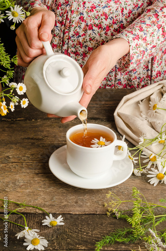Woman pouring chamomile herbal tea on dark wooden background