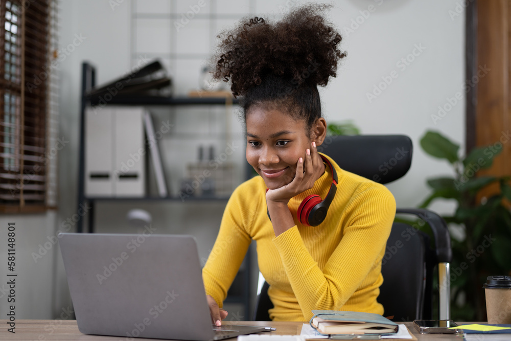 Lovely african american woman sitting at desk working on laptop computer in her comfortable office room. Lovely african american woman sitting at desk working on laptop computer in her comfortable office room.