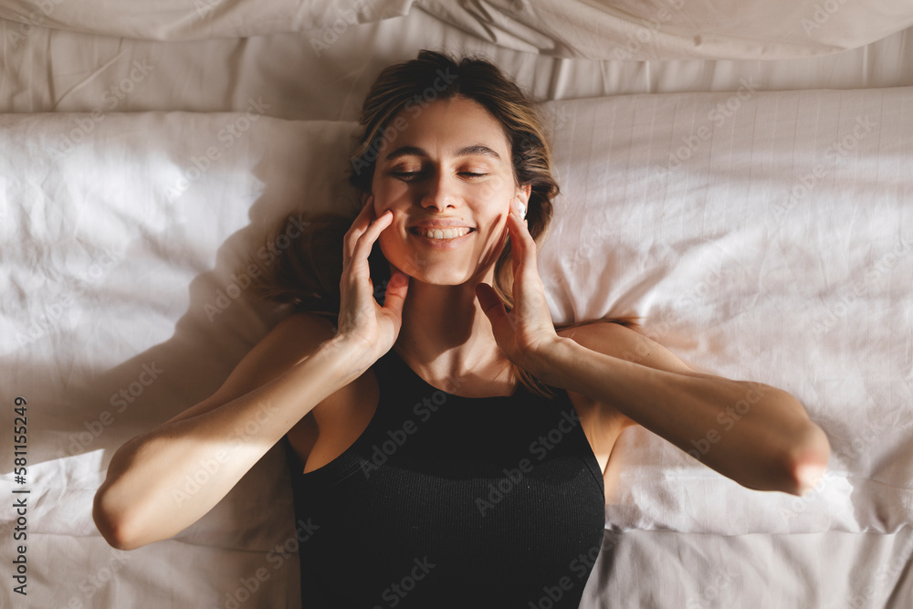Naklejka premium Beautiful young woman listening music in wireless headphones at home lying on bed. Young pretty woman person are happy and enjoy with music by using earphone for listen a sound audio in bedroom.