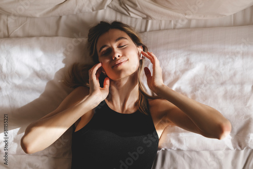 Beautiful young woman listening music in wireless headphones at home lying on bed. Young pretty woman person are happy and enjoy with music by using earphone for listen a sound audio in bedroom.