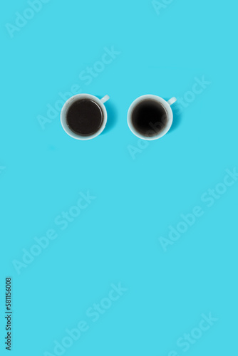 Two coffee cups give the shape of eyes on a blue background. Creative minimal concept.