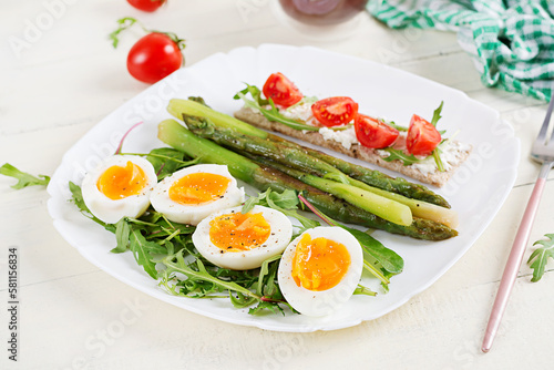 Green asparagus with boiled eggs and sandwich cream cheese on a white plate.