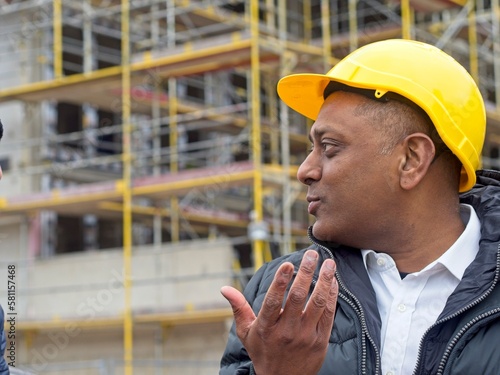 Profile portrait of an Indian civil engineer or factory worker wearing a safety helmet looking aside gesturing