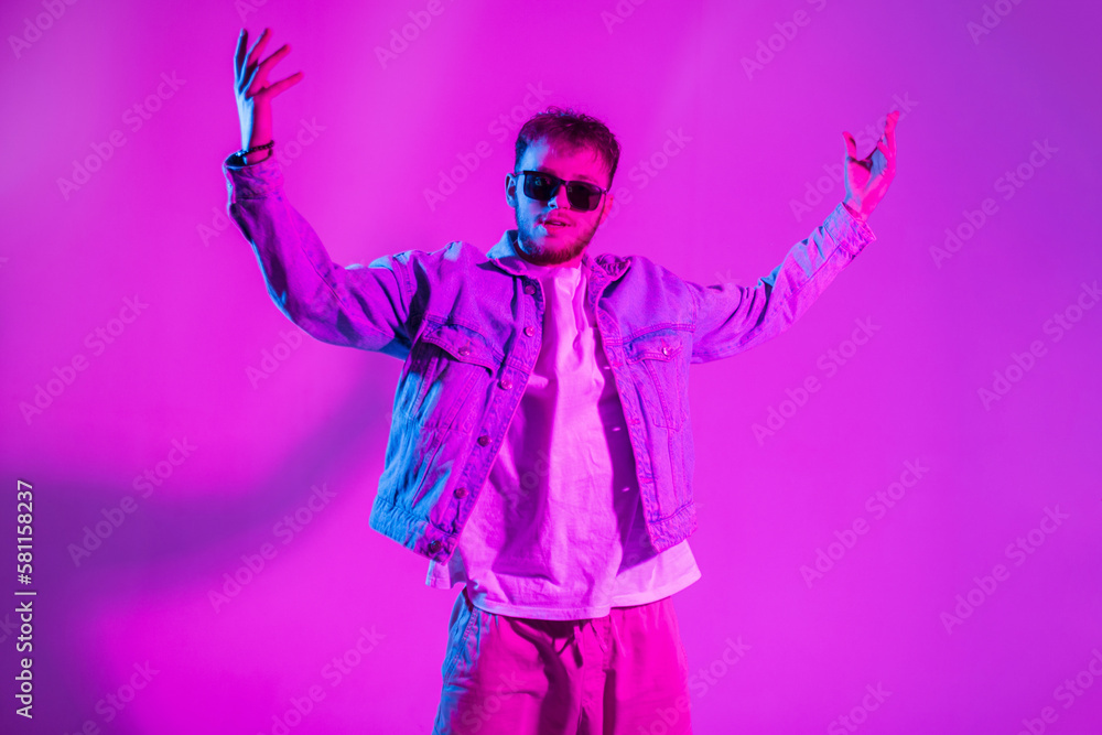 Creative handsome fashion dancer man with sunglasses in stylish denim clothes dance in colorful studio with pink and neon light Creative handsome fashion dancer man with sunglasses in stylish denim clothes dance in colorful studio with pink and neon light