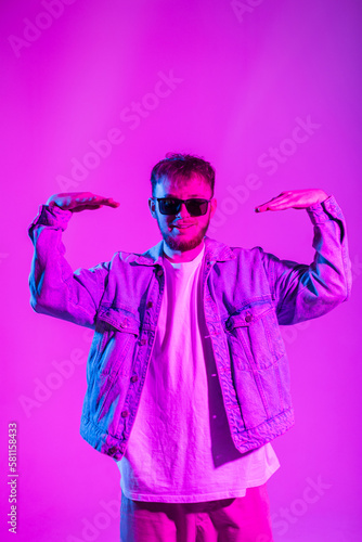 Handsome stylish young man hipster dancer in fashion trendy clothes with denim jacket and sunglasses is dancing in creative studio with pink and blue light © alones