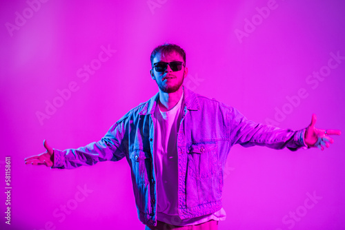 Fashion hip hop dancer handsome guy in stylish casual denim clothes with black sunglasses dancing in the studio with creative pink and blue light